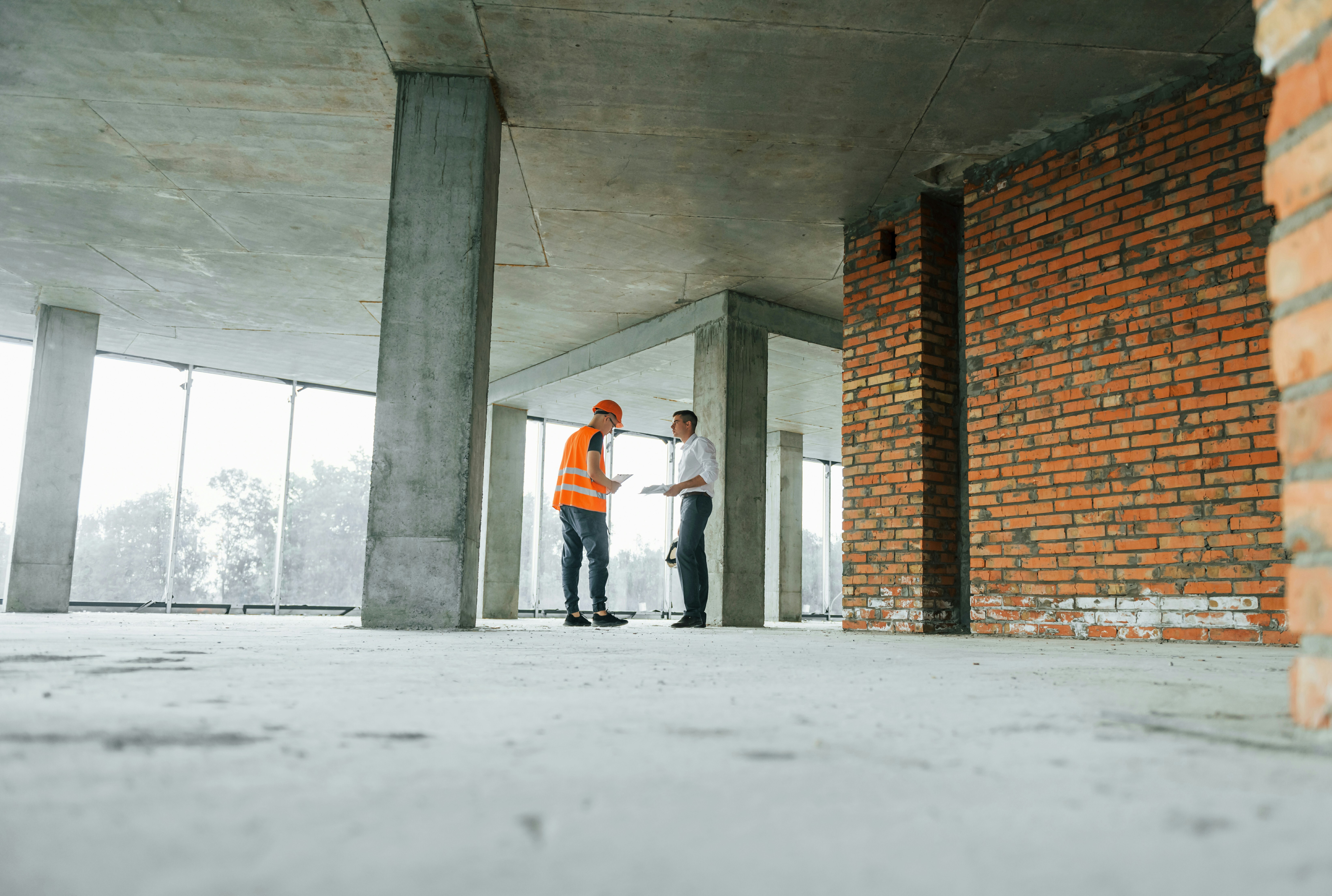 Arkitekt och byggledare med hjälmar granskar ritningar i nybyggt hus.jpg